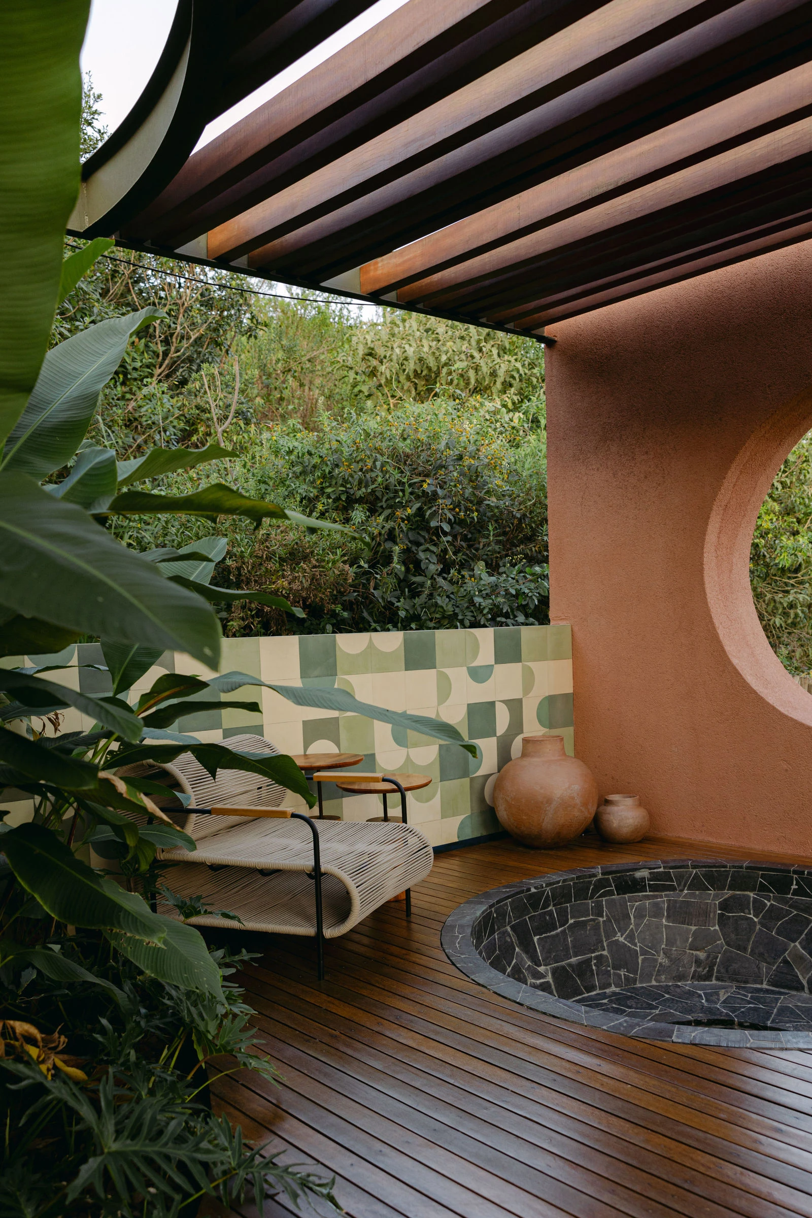 Deck do spa com ofurô de pedra, pergolado e azulejos verdes geométricos