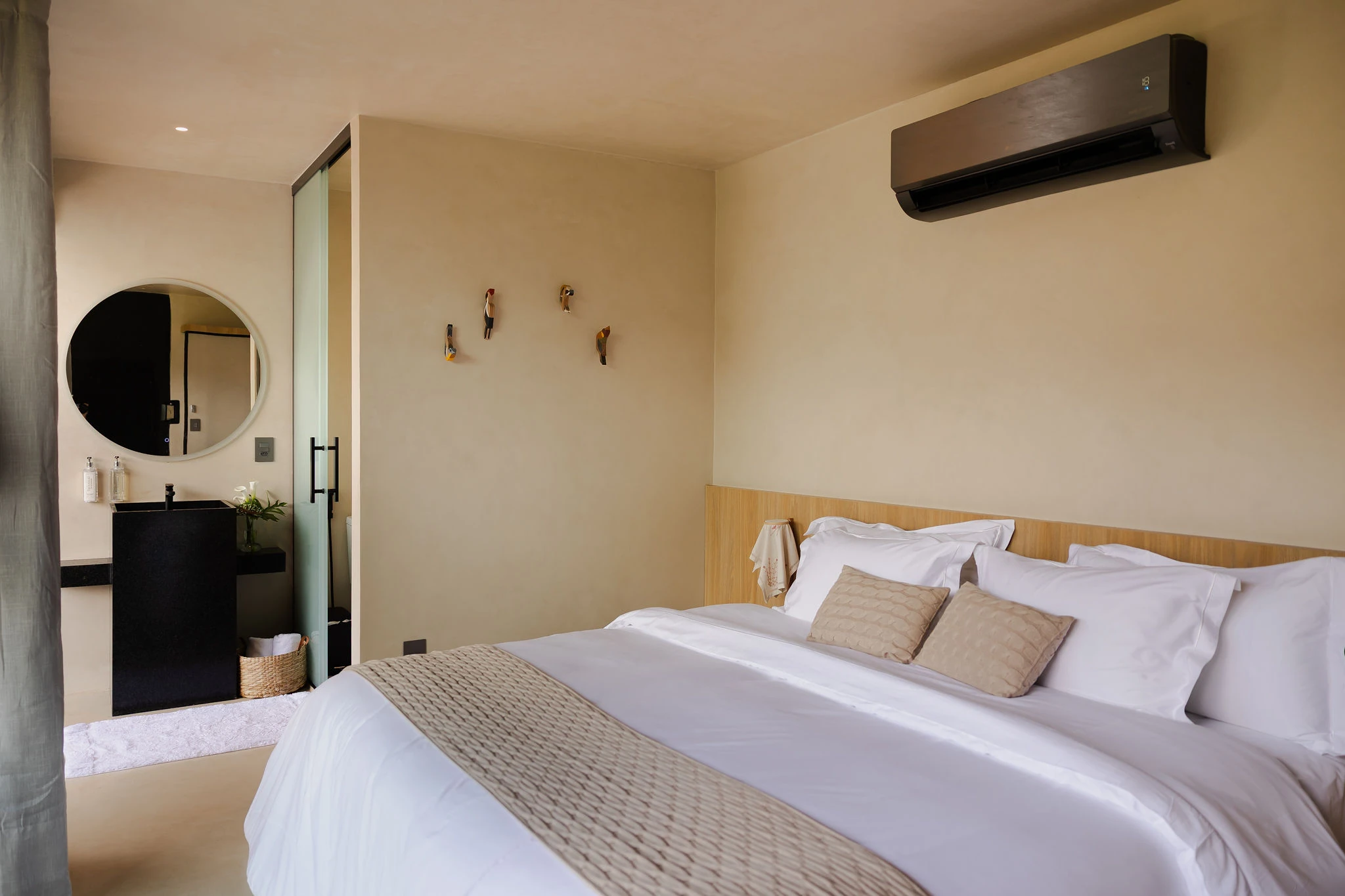 Quarto da Suíte Superior com cama king, pássaros de madeira na parede e banho ao fundo