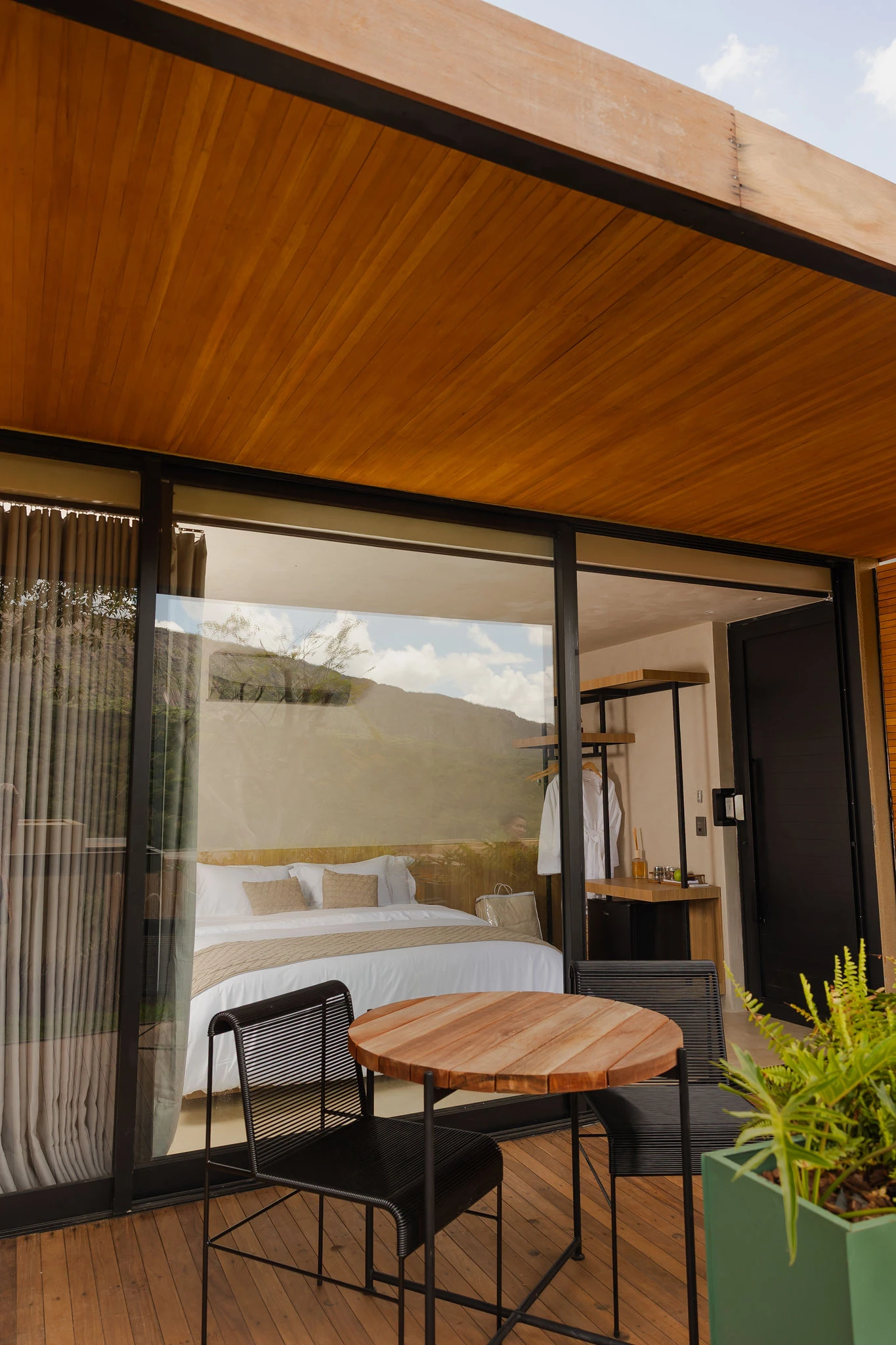 Varanda da Suíte Superior com mesa de madeira e o quarto ao fundo